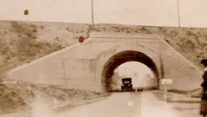 Concrete railroad bridge over road with 1930s car approaching through underpass